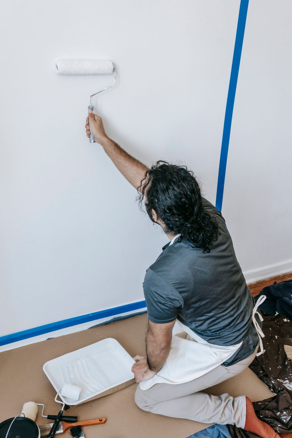 A painter seen from behind rolling fresh paint onto an interior wall.